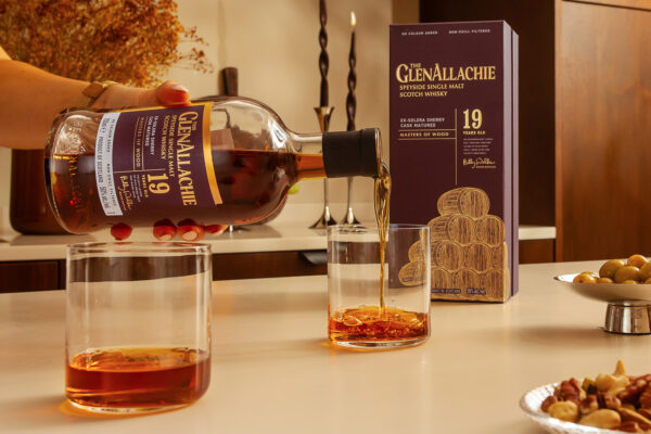 jemand schenkt den The GlenAllachie 19 Jahre Ex-Solera Sherry Cask Matured in Gläser ein. Auf dem Tisch zudem Snacks