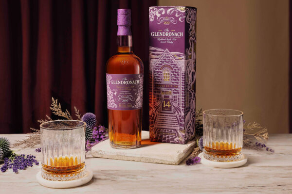 eine Flasche The Glendronach 14 Jahre Boynsmill House Edition samt Geschenkverpackung steht auf einem Steintisch. Um sie herum Kräuter und Gläser