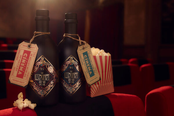 The Illusionist Distiller’s Edition 2026 zwei Flaschen Gin und eine Tüte Popcorn stehen auf einem Sessel in einem Kinosaal