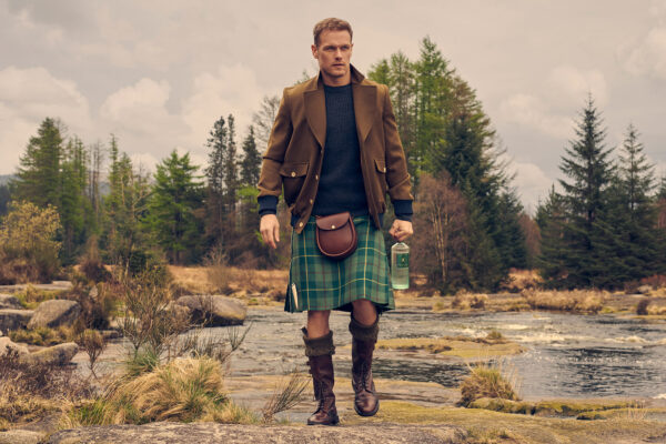 Sam Heughan das Foto zeigt Sam Heughan in der schottischen Wildnis mit einer Flasche The ’Nach Wild Scottish Gin in der Hand