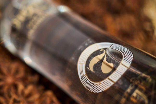 Thracian Ouzo 7 Gold eine diagonal auf Sternanis liegende Flasche Thracian Ouzo 7 Gold. Der Fokus liegt auf dem Etikett mit der Zahl "7"