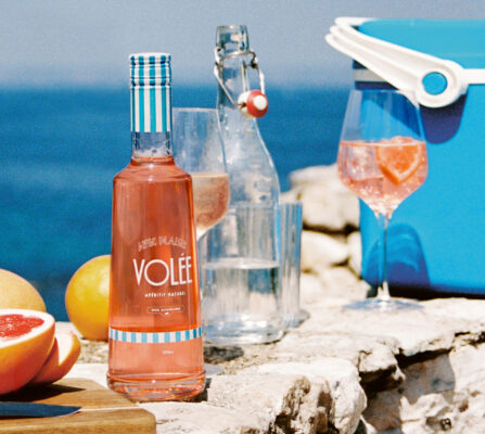 Volée Apéritif Naturel eine Flasche Volée Apéritif Naturel, mehrere Drinks und Zitrusfrüchte auf einer Mauer am Meer