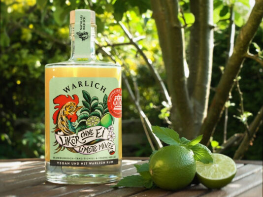 eine Flasche Warlich Likör ohne Ei Limette & Minze nebst Limetten und Minze auf einem Gartentisch